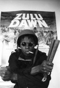 Black militant John Taylor poses in front of a poster for the movie 'Zulu Dawn' London 1987