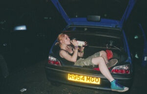 Woman drinks from a bottle sat in a car boot, UK, 2000s